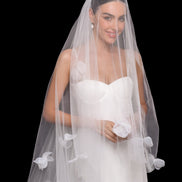 Bride wearing a white wedding dress with a floral veil against a black background