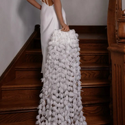 Woman in a white gown with a floral train standing on wooden stairs.