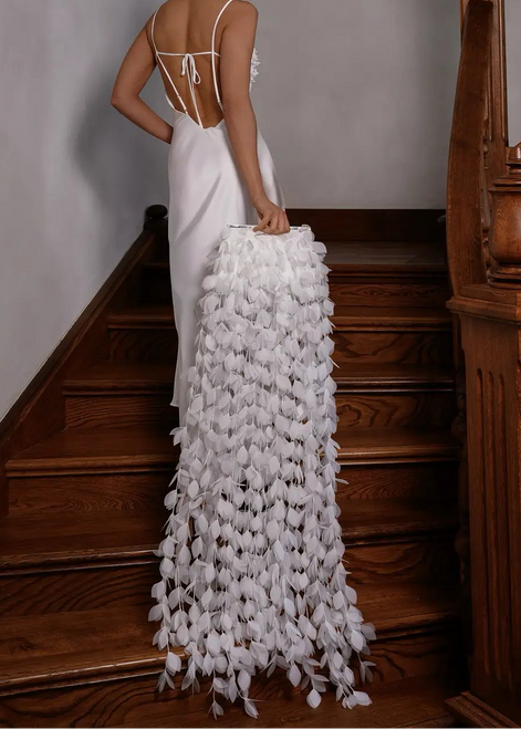 Woman in a white gown with a floral train standing on wooden stairs.
