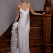 Woman in a white evening gown with floral details standing on a staircase.