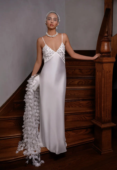 Woman in a white evening gown with floral details standing on a staircase.