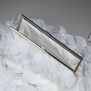 Silver clutch on a bed of white feathers with a gray background