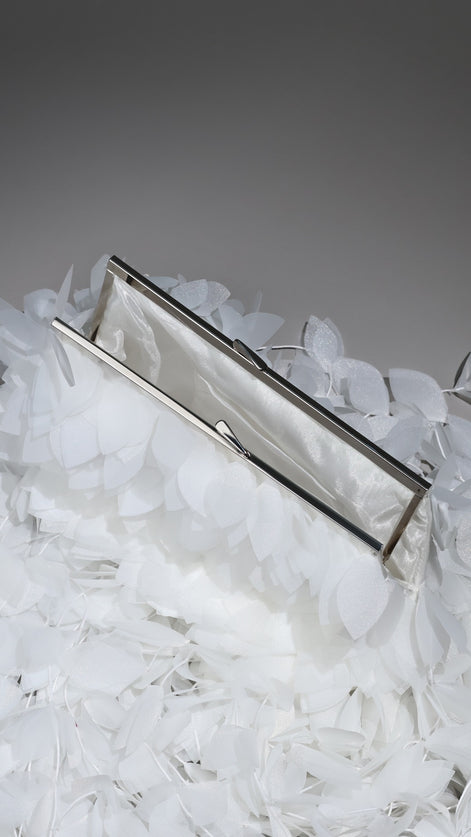Silver clutch on a bed of white feathers with a gray background
