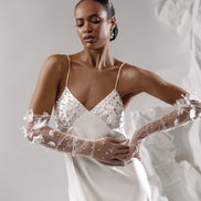 Woman in a white wedding dress with lace gloves against a neutral background