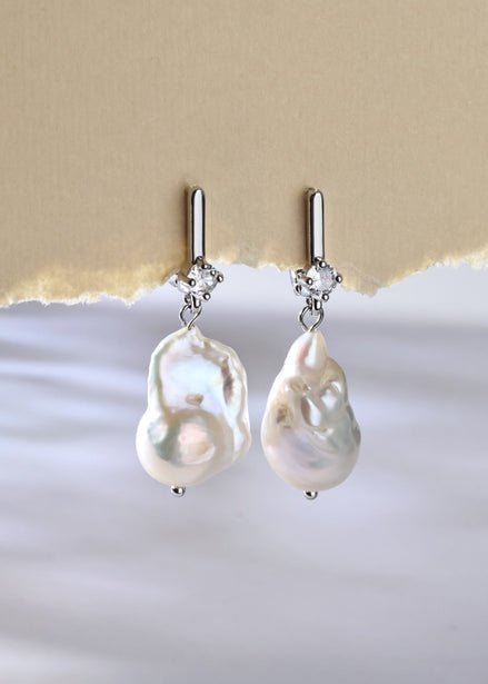 Pearl earrings with silver hooks on a textured beige and white background