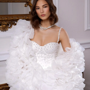 Woman wearing a white wedding dress with ruffled sleeves in an elegant interior setting.