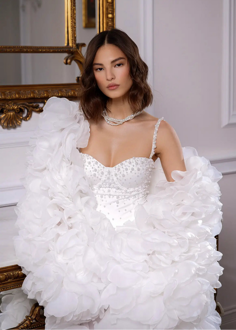Woman wearing a white wedding dress with ruffled sleeves in an elegant interior setting.