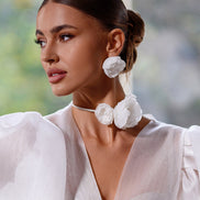Woman wearing large white floral earrings and a white outfit with a blurred natural background