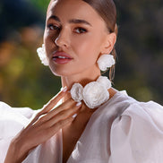 Woman wearing white floral earrings with a blurred green background