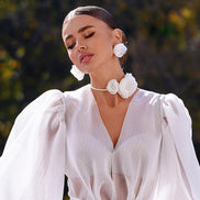 Woman wearing a white dress with floral accessories against a blurred natural background