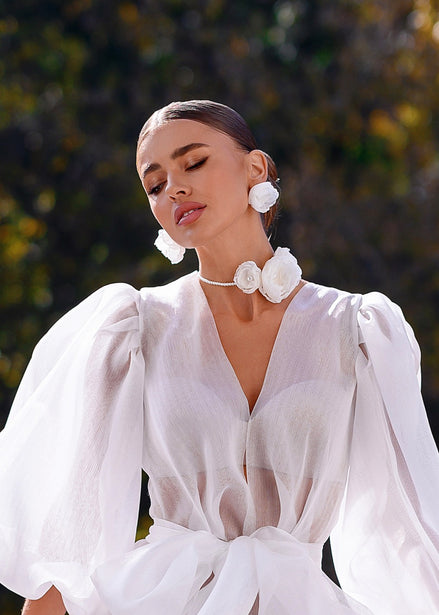 Woman wearing a white dress with floral accessories against a blurred natural background