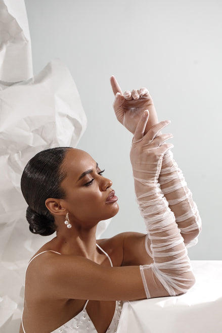 Woman wearing a white dress with sheer gloves against a light background