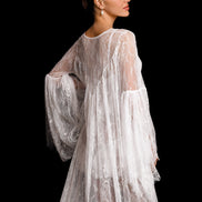 Woman wearing a sheer, embroidered white dress against a black background