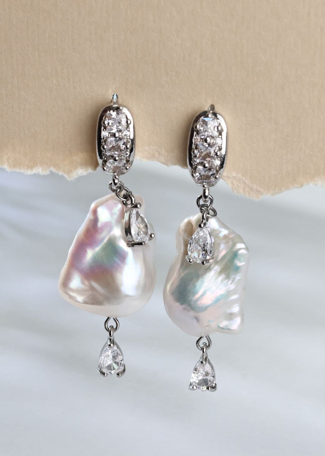 Pearl and crystal earrings on a textured beige and white background