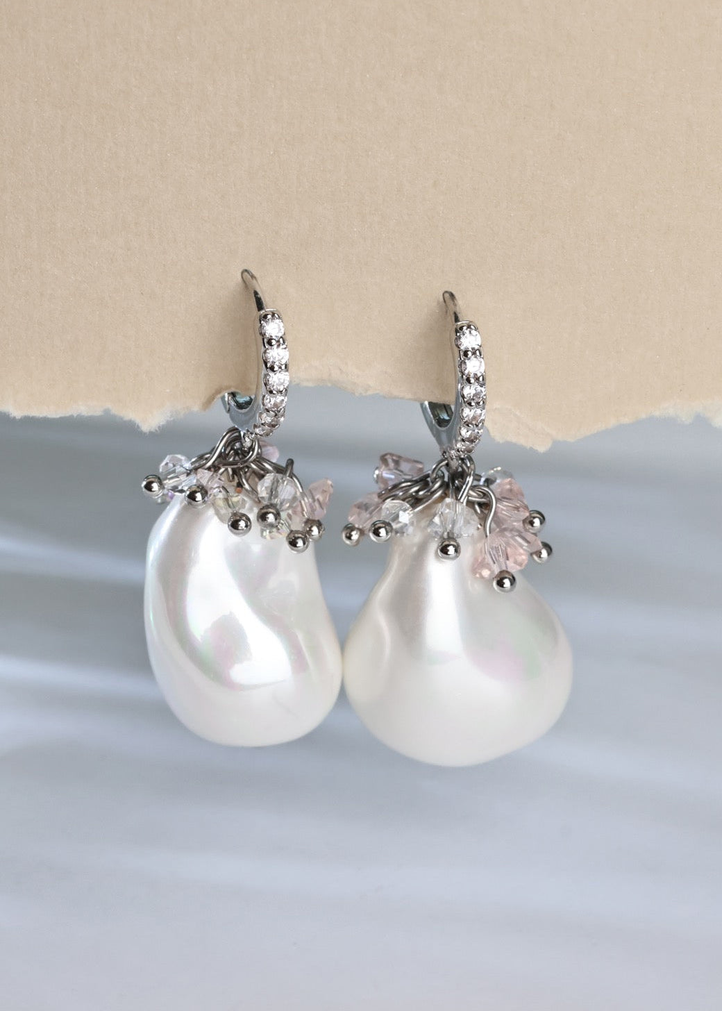 Pearl earrings with silver and pink accents on a light blue and beige background