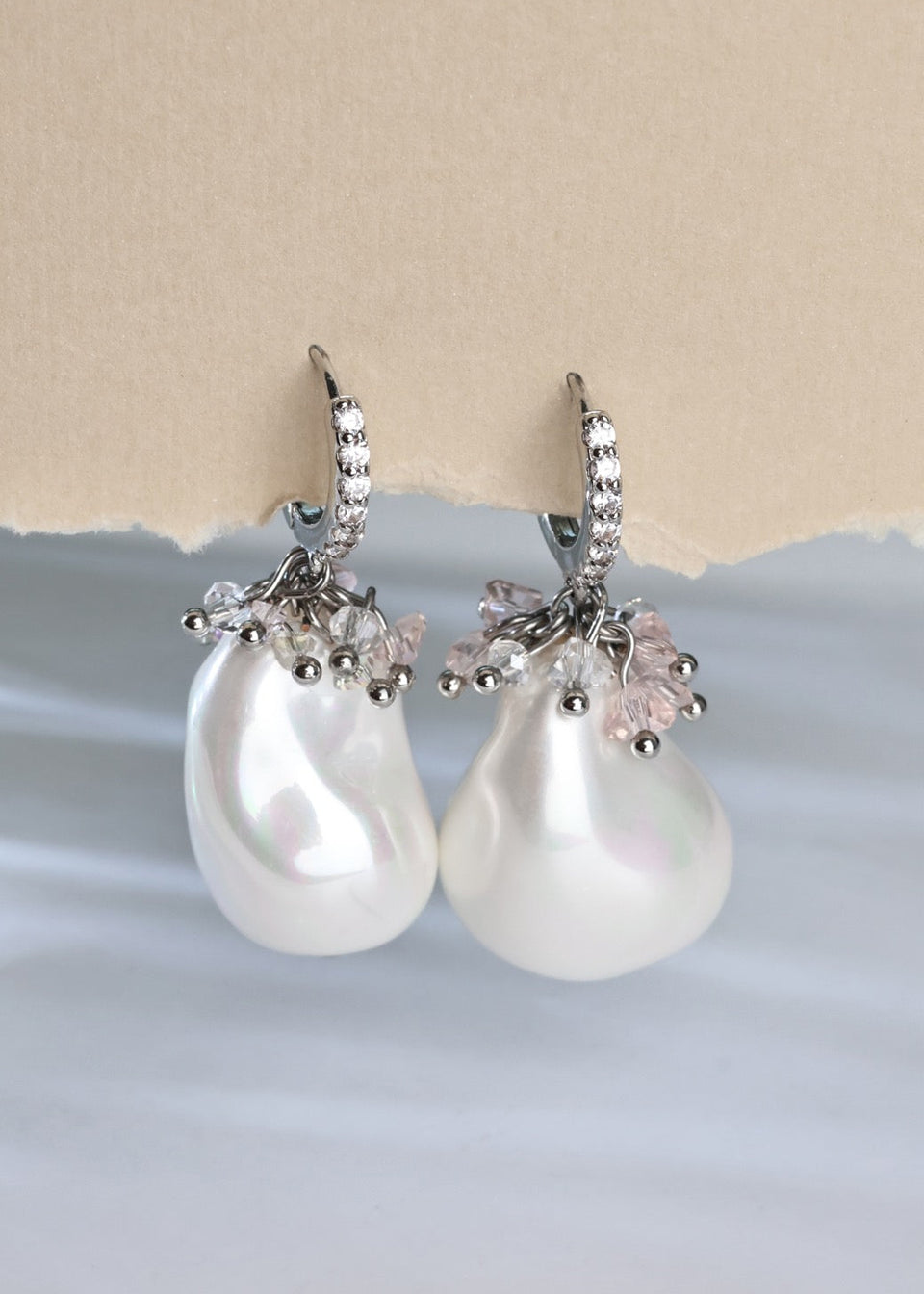Pearl earrings with silver and pink accents on a light blue and beige background