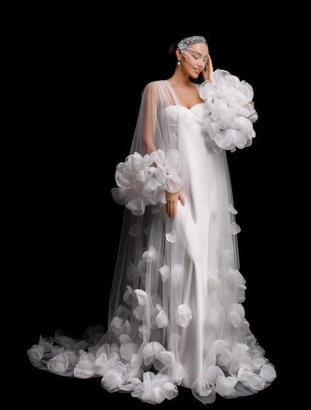 Woman in a white wedding dress with floral details against a black background