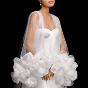 Woman in a white wedding dress holding a large white bouquet against a black background