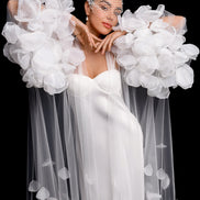 Woman in a white dress with floral sleeves against a black background