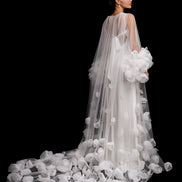 Bride in a white wedding gown with a long train and floral details against a black background