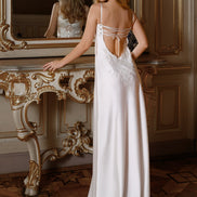Woman in a white evening gown standing in a room with ornate decor.