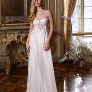 Woman in a white evening gown standing in an elegant room with gold accents and large windows.