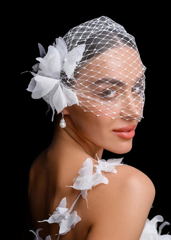 Woman wearing a birdcage veil with white flowers against a black background