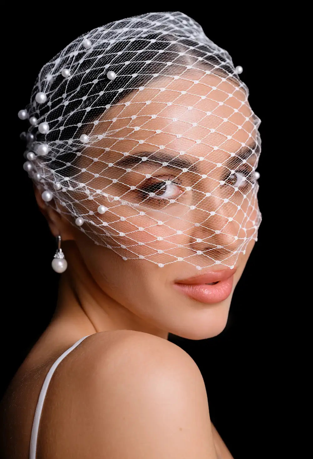 Woman wearing a birdcage veil with pearls on a black background