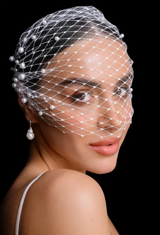 Woman wearing a birdcage veil with pearls on a black background