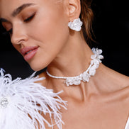 Woman wearing white floral earrings and a matching necklace with a black background